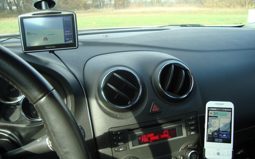 A handset clipped to a dashboard mount, running navigation next to a separate satnav unit.